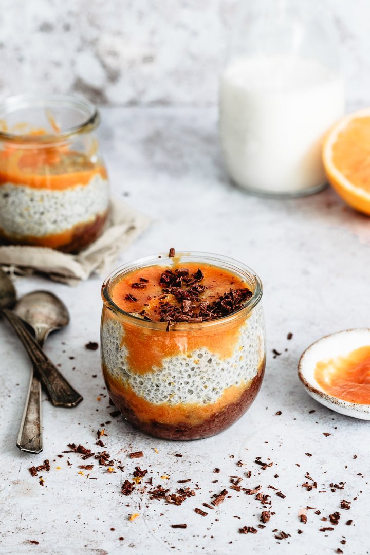 Chocolate chia pudding with orange purée served in a glass jar with spoons aside