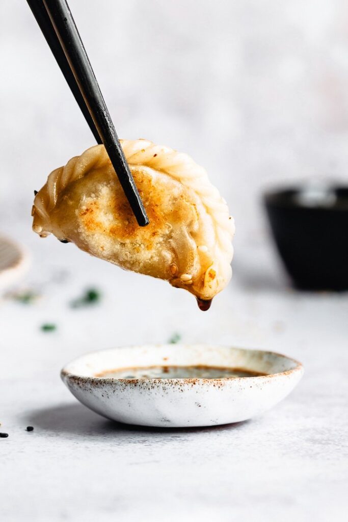 A single vegan potsticker dipped in its sauce.