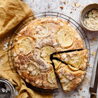 Sliced ricotta cake with lemon on a cooling rack, with a yellow napkin next to it.