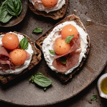 A plate with three pieces of bread with prosciutto and melon, and goat cheese.