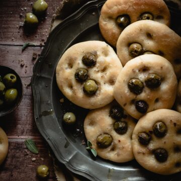 Mini focaccias with olives on top, on a round tray.