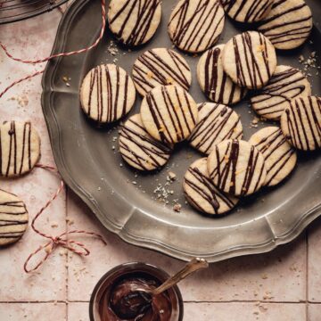 A lot of chocolate orange shortbread cookies on a vintage serving tray and a glass with melted chocolate next to it.